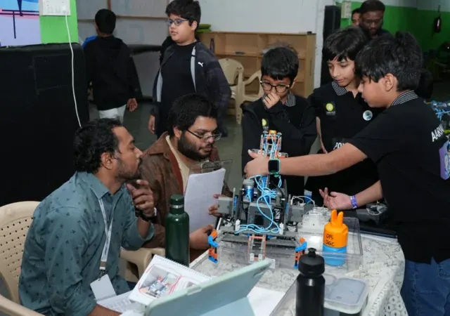 Students showing their robot to two judges across a table, with build notes and a laptop between them