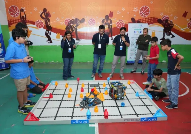 Students at the controls around a VEX IQ regional competition field, with coaches and judges watching from the side