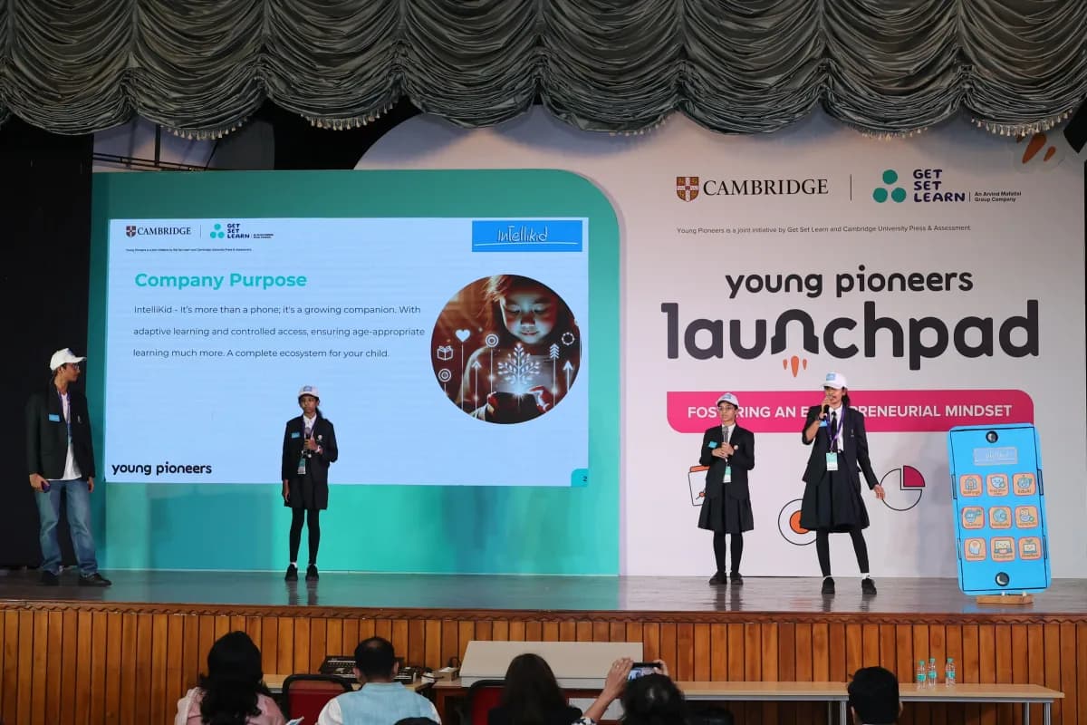 Two students presenting their venture on stage at the Young Pioneers Launchpad, in front of a Cambridge and Get Set Learn backdrop